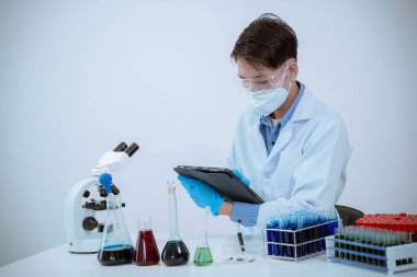 Laboratuvarda çalışan bir bilim adamı mikroskop ile laboratuarda mavi sıvıyla dolu bir test tüpü tutuyor. Muayene. Tıbbi araştırma.