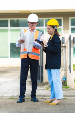 İki erkek ve kadın mimari mühendisi önünde dizüstü bilgisayarlar olan bir binaya bakıyor. Güvenlik teçhizatı takıyorlar ve bir binayı işaret ediyorlar. Dikey resim