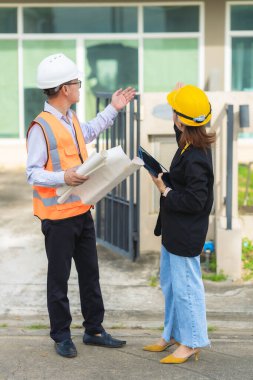 İki erkek ve kadın mimari mühendisi önünde dizüstü bilgisayarlar olan bir binaya bakıyor. Güvenlik teçhizatı takıyorlar ve bir binayı işaret ediyorlar. Dikey resim