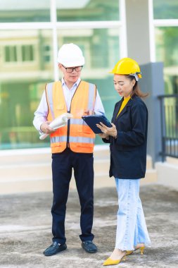İki erkek ve kadın mimari mühendisi önünde dizüstü bilgisayarlar olan bir binaya bakıyor. Güvenlik teçhizatı takıyorlar ve bir binayı işaret ediyorlar. Dikey resim