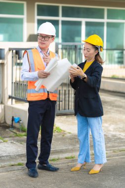İki erkek ve kadın mimari mühendisi önünde dizüstü bilgisayarlar olan bir binaya bakıyor. Güvenlik teçhizatı takıyorlar ve bir binayı işaret ediyorlar. Dikey resim