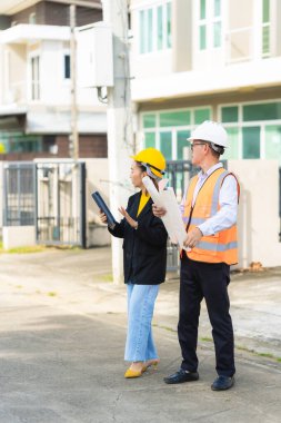 İki erkek ve kadın mimari mühendisi önünde dizüstü bilgisayarlar olan bir binaya bakıyor. Güvenlik teçhizatı takıyorlar ve bir binayı işaret ediyorlar. Dikey resim