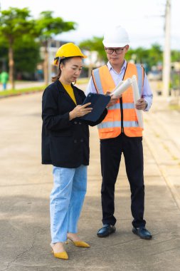 İki erkek ve kadın mimari mühendisi önünde dizüstü bilgisayarlar olan bir binaya bakıyor. Güvenlik teçhizatı takıyorlar ve bir binayı işaret ediyorlar. Dikey resim