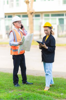 İki erkek ve kadın mimari mühendisi önünde dizüstü bilgisayarlar olan bir binaya bakıyor. Güvenlik teçhizatı takıyorlar ve bir binayı işaret ediyorlar. Dikey resim