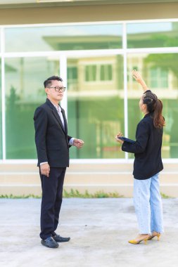 İnşaat sırasında takım elbiseli yakışıklı bir emlakçı evin önünde duruyor ve bir müşteriden randevu almak için tablet kullanıyor. Dikey resim