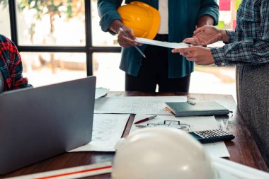 Endüstriyel mühendislerden oluşan bir ekip, makine planlarını analiz etmek için toplanıyor. Projeyi masada tartışın, ofisteki bina tasarımı projesini çizmek için dizüstü bilgisayarı kullanın. inşaat kavramı
