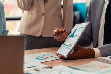 Piyasa verilerini, bilançolarını, muhasebe ve net kazanç tablosunu analiz etmek üzere grafik ve grafiklere işaret eden iş adamlarından oluşan bir iş sunumu veya seminer grubunda evrak işleri ve eller masanın üzerinde..