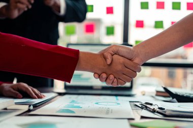 Girişimcilerin işbirliği anlaşması, modern ofiste hesap makinesi ve finansal belgelerle başarılı bir iş anlaşmasını sembolize eden ahşap masa üzerinde el sıkışıyor..