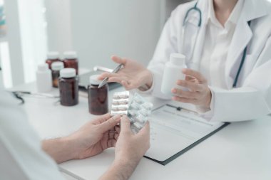 Genç Asyalı bir adam, sağlık sorunlarını tartışmak ve açıklamak için tıp bürosunda kadın doktorla görüşüyor. Doktor ve hasta birlikte muayene odasında bir masada oturuyorlar..