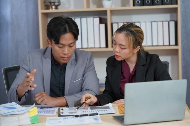 İki genç Asyalı iş adamı, başarılı bir girişim için beyin fırtınası yapmak amacıyla bir konferans odasında iş konularını tartışıyor. Ofisteki dizüstü bilgisayarlarla birlikte çalışmak