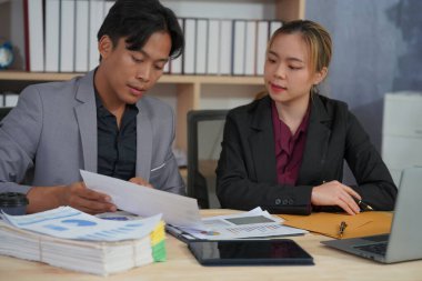 İki genç Asyalı iş adamı, başarılı bir girişim için beyin fırtınası yapmak amacıyla bir konferans odasında iş konularını tartışıyor. Ofisteki dizüstü bilgisayarlarla birlikte çalışmak