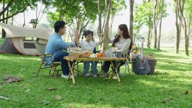 Mutlu Asyalı aile parkta kamp yapıyor, dışarıda eğleniyor, bir tatil partisini kutluyor, yemek yiyor, gitar çalıyor ve birlikte şarkı söylüyor..