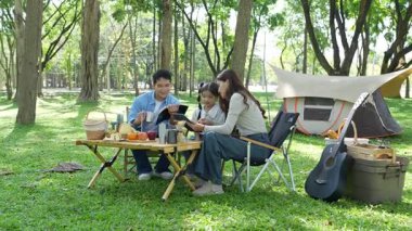 Mutlu Asyalı aile parkta kamp yapıyor, dışarıda eğleniyor, bir tatil partisini kutluyor, yemek yiyor, gitar çalıyor ve birlikte şarkı söylüyor..