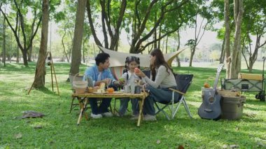 Mutlu Asyalı aile parkta kamp yapıyor, dışarıda eğleniyor, bir tatil partisini kutluyor, yemek yiyor, gitar çalıyor ve birlikte şarkı söylüyor..