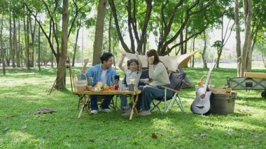 Mutlu Asyalı aile parkta kamp yapıyor, dışarıda eğleniyor, bir tatil partisini kutluyor, yemek yiyor, gitar çalıyor ve birlikte şarkı söylüyor..