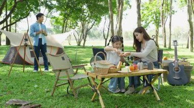 Mutlu Asyalı aile parkta kamp yapıyor, dışarıda eğleniyor, bir tatil partisini kutluyor, yemek yiyor, gitar çalıyor ve birlikte şarkı söylüyor..