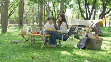 Mutlu Asyalı aile parkta kamp yapıyor, dışarıda eğleniyor, bir tatil partisini kutluyor, yemek yiyor, gitar çalıyor ve birlikte şarkı söylüyor..