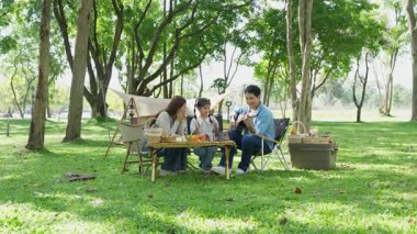 Mutlu Asyalı aile parkta kamp yapıyor, dışarıda eğleniyor, bir tatil partisini kutluyor, yemek yiyor, gitar çalıyor ve birlikte şarkı söylüyor..