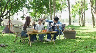 Mutlu Asyalı aile parkta kamp yapıyor, dışarıda eğleniyor, bir tatil partisini kutluyor, yemek yiyor, gitar çalıyor ve birlikte şarkı söylüyor..
