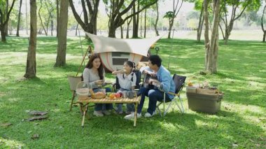 Mutlu Asyalı aile parkta kamp yapıyor, dışarıda eğleniyor, bir tatil partisini kutluyor, yemek yiyor, gitar çalıyor ve birlikte şarkı söylüyor..
