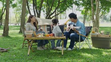 Mutlu Asyalı aile parkta kamp yapıyor, dışarıda eğleniyor, bir tatil partisini kutluyor, yemek yiyor, gitar çalıyor ve birlikte şarkı söylüyor..