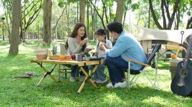 Mutlu Asyalı aile parkta kamp yapıyor, dışarıda eğleniyor, bir tatil partisini kutluyor, yemek yiyor, gitar çalıyor ve birlikte şarkı söylüyor..