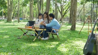 Mutlu Asyalı aile parkta kamp yapıyor, dışarıda eğleniyor, bir tatil partisini kutluyor, yemek yiyor, gitar çalıyor ve birlikte şarkı söylüyor..