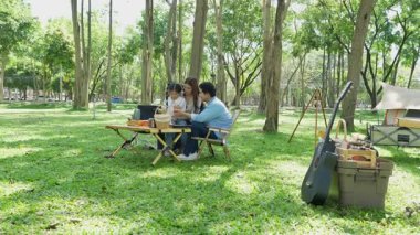 Mutlu Asyalı aile parkta kamp yapıyor, dışarıda eğleniyor, bir tatil partisini kutluyor, yemek yiyor, gitar çalıyor ve birlikte şarkı söylüyor..