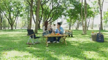 Mutlu Asyalı aile parkta kamp yapıyor, dışarıda eğleniyor, bir tatil partisini kutluyor, yemek yiyor, gitar çalıyor ve birlikte şarkı söylüyor..