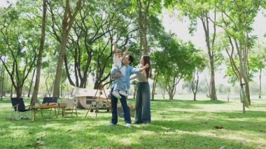 Mutlu Asyalı aile parkta kamp yapıyor, dışarıda eğleniyor, bir tatil partisini kutluyor, yemek yiyor, gitar çalıyor ve birlikte şarkı söylüyor..