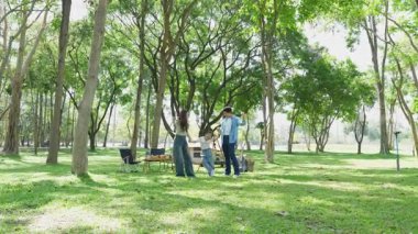 Mutlu Asyalı aile parkta kamp yapıyor, dışarıda eğleniyor, bir tatil partisini kutluyor, yemek yiyor, gitar çalıyor ve birlikte şarkı söylüyor..