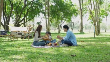 Mutlu Asyalı aile parkta kamp yapıyor, dışarıda eğleniyor, bir tatil partisini kutluyor, yemek yiyor, gitar çalıyor ve birlikte şarkı söylüyor..