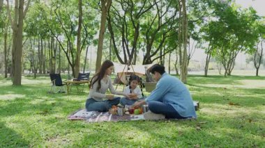 Mutlu Asyalı aile parkta kamp yapıyor, dışarıda eğleniyor, bir tatil partisini kutluyor, yemek yiyor, gitar çalıyor ve birlikte şarkı söylüyor..