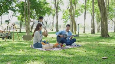 Mutlu Asyalı aile parkta kamp yapıyor, dışarıda eğleniyor, bir tatil partisini kutluyor, yemek yiyor, gitar çalıyor ve birlikte şarkı söylüyor..