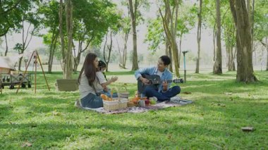 Mutlu Asyalı aile parkta kamp yapıyor, dışarıda eğleniyor, bir tatil partisini kutluyor, yemek yiyor, gitar çalıyor ve birlikte şarkı söylüyor..