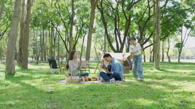 Mutlu Asyalı aile parkta kamp yapıyor, dışarıda eğleniyor, bir tatil partisini kutluyor, yemek yiyor, gitar çalıyor ve birlikte şarkı söylüyor..