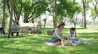 Mutlu Asyalı aile parkta kamp yapıyor, dışarıda eğleniyor, bir tatil partisini kutluyor, yemek yiyor, gitar çalıyor ve birlikte şarkı söylüyor..