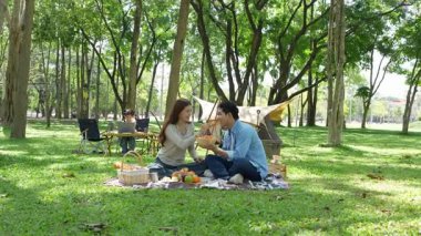 Mutlu Asyalı aile parkta kamp yapıyor, dışarıda eğleniyor, bir tatil partisini kutluyor, yemek yiyor, gitar çalıyor ve birlikte şarkı söylüyor..