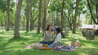 Mutlu Asyalı aile parkta kamp yapıyor, dışarıda eğleniyor, bir tatil partisini kutluyor, yemek yiyor, gitar çalıyor ve birlikte şarkı söylüyor..