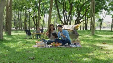 Mutlu Asyalı aile parkta kamp yapıyor, dışarıda eğleniyor, bir tatil partisini kutluyor, yemek yiyor, gitar çalıyor ve birlikte şarkı söylüyor..