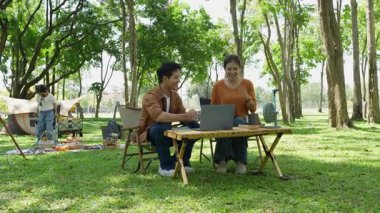 Mutlu Asyalı aile parkta kamp yapıyor, dışarıda eğleniyor, bir tatil partisini kutluyor, yemek yiyor, gitar çalıyor ve birlikte şarkı söylüyor..