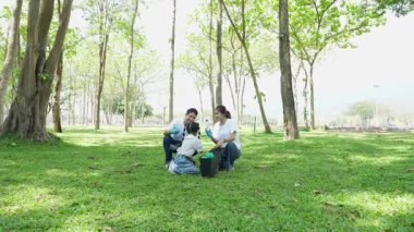 Babaları, anneleri ve çocukları olan Asyalı bir aile parkta çöp topluyor. Doğada, çocuklarınıza doğayı ve çevreyi sevmeyi öğretin..
