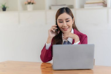 Hesap makinesiyle çalışan ve finansal belgeleri analiz eden gülümseyen Asyalı muhasebeci. Ve bir masadaki dizüstü bilgisayarda çalışmak.