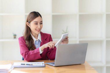 Hesap makinesiyle çalışan ve finansal belgeleri analiz eden gülümseyen Asyalı muhasebeci. Ve bir masadaki dizüstü bilgisayarda çalışmak.