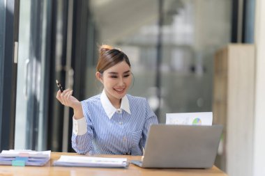 Hesap makinesiyle çalışan ve finansal belgeleri analiz eden gülümseyen Asyalı muhasebeci. Ve bir masadaki dizüstü bilgisayarda çalışmak.