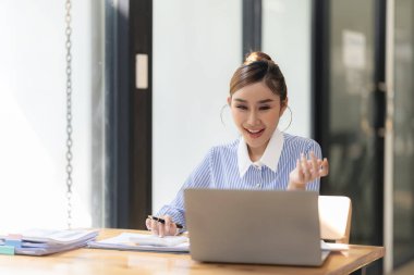 Hesap makinesiyle çalışan ve finansal belgeleri analiz eden gülümseyen Asyalı muhasebeci. Ve bir masadaki dizüstü bilgisayarda çalışmak.