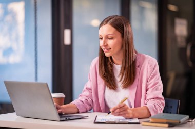 Masasında dizüstü bilgisayar ve belgelerle çalışan genç bir muhasebeci, gece geç saatlere kadar çalışıyor, araştırıyor, rapor ediyor ve mesai saatlerini ayarlıyor..