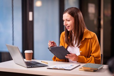Masasında dizüstü bilgisayar ve belgelerle çalışan genç bir muhasebeci, gece geç saatlere kadar çalışıyor, araştırıyor, rapor ediyor ve mesai saatlerini ayarlıyor..