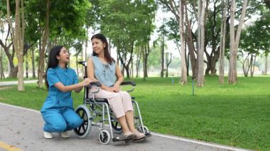 Tekerlekli sandalyede oturan ve parkta kadın bir hemşire tarafından bakılan yaşlı bir kadın. Doğal terapi konsepti. Ya da yaşlıların bakıcıları.