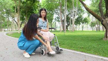 Tekerlekli sandalyede oturan ve parkta kadın bir hemşire tarafından bakılan yaşlı bir kadın. Doğal terapi konsepti. Ya da yaşlıların bakıcıları.